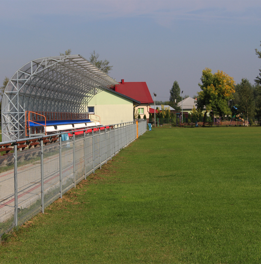 Sokolniki. Stadion sportowy. Po lewej stronie zadaszone trybuny, w tle budynek bo prawej stronie boisko trawiaste