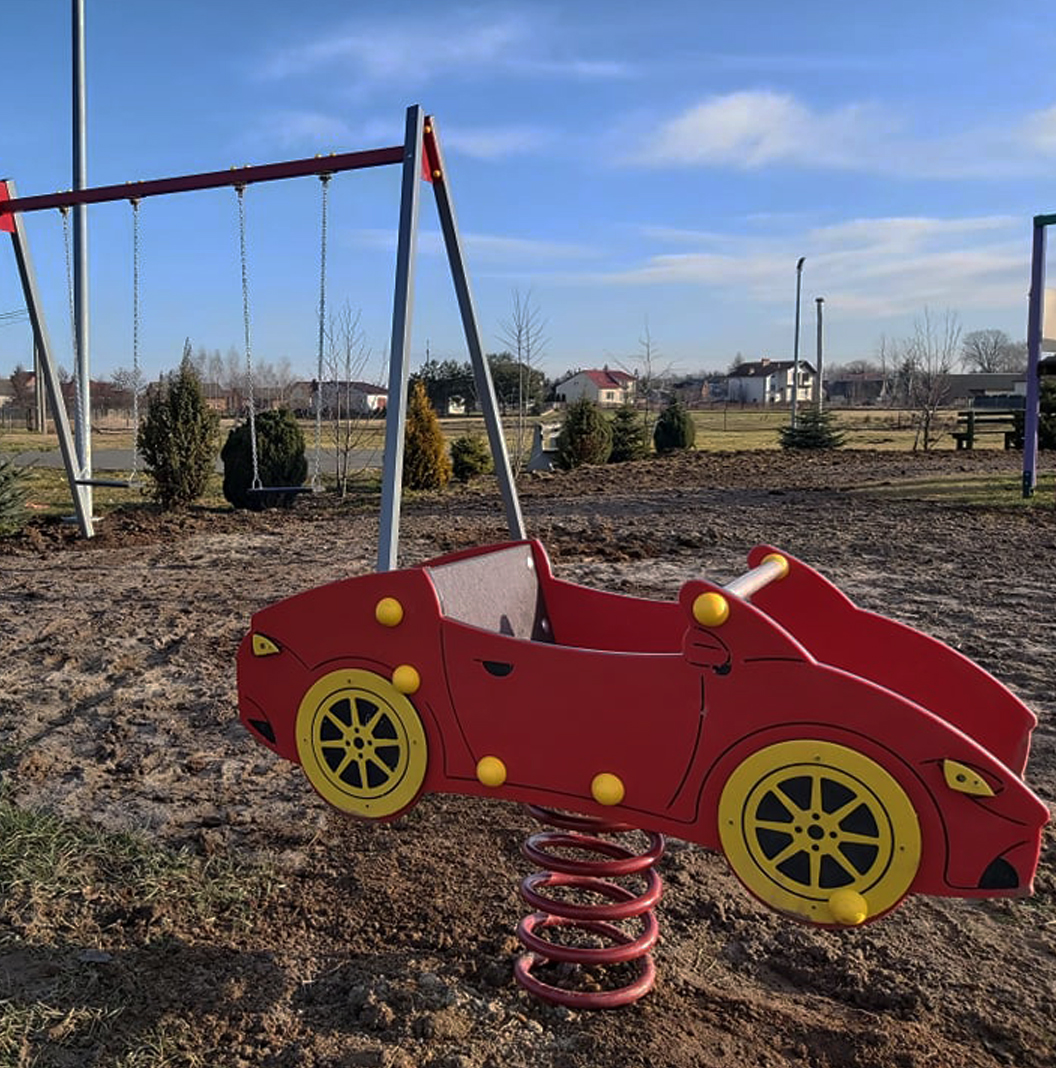 Sokolniki. Plac zabaw dla dzieci, na pierwszym planie bujak w kształcie czerwonego samochodziki, w tle po lewej stronie huśtawki